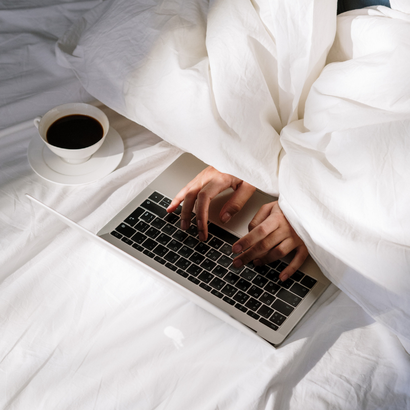 Hands typing on laptop in bed